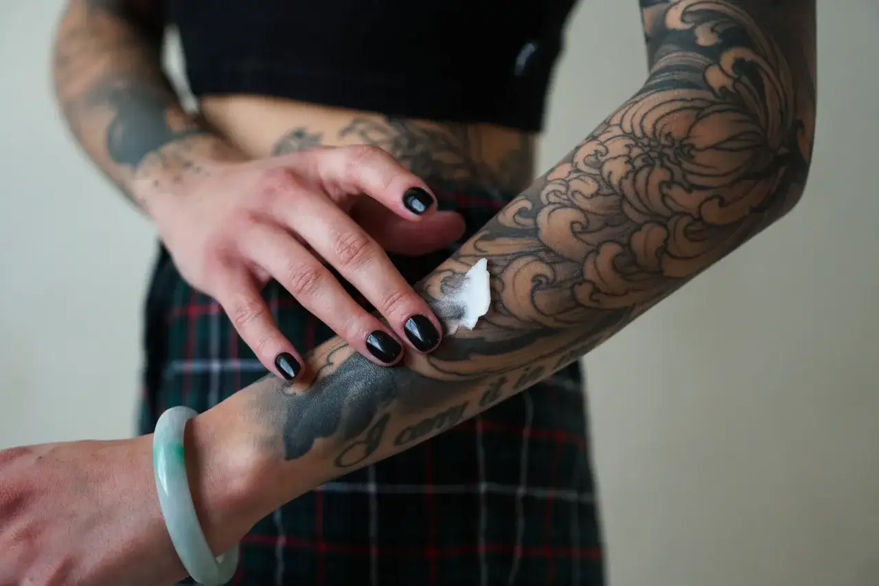 Frau tr&auml;gt nach dem Tattoo danach eine wei&szlig;e Creme auf ihren t&auml;towierten Arm auf.