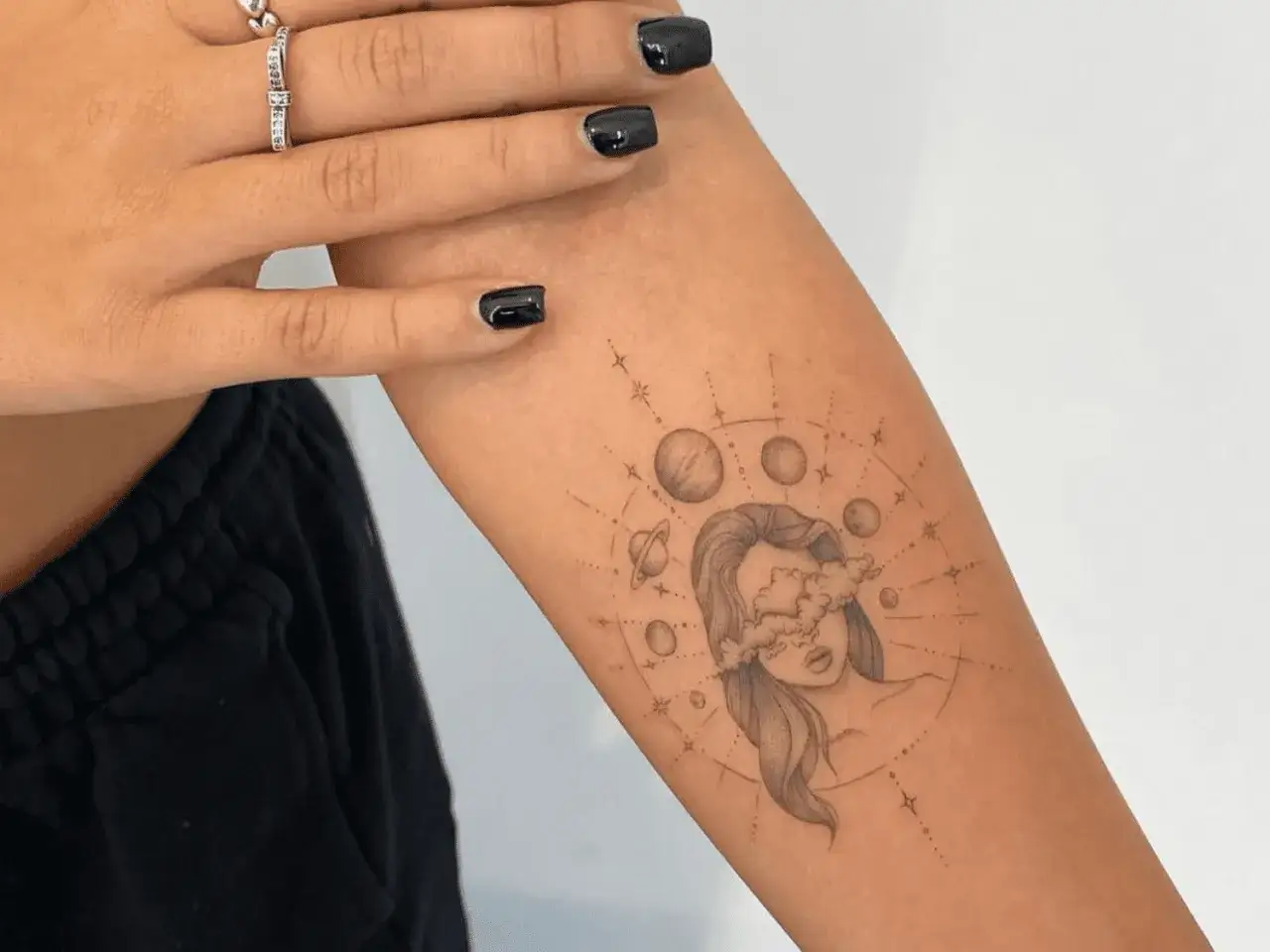 Ein feminines Tattoo mit einem Kompass-Motiv: Eine Frau mit Wolken vor den Augen, umgeben von Planeten und Sternen.