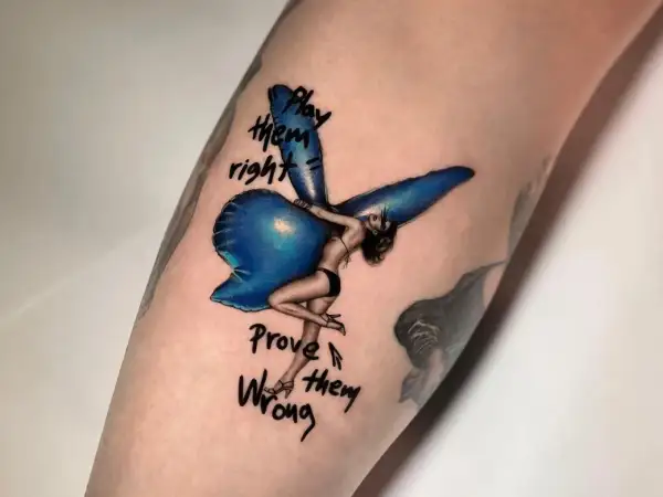 Ein Fineline Tattoo zeigt eine Frau mit Flügeln, die auf einem blauen Ballon sitzt. Darunter steht "Play them right, Prove them wrong".