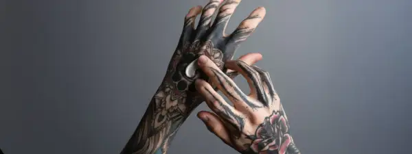 Hände mit detaillierten Tätowierungen, die sich eincremen. Das Tattoo rot nach stechen ist noch leicht zu erkennen.
