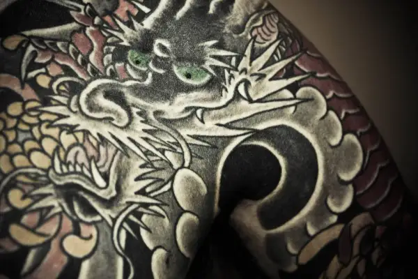 Ein detailreiches Irezumi Tattoo zeigt einen Drachenkopf mit grünen Augen, der sich über die Haut schlängelt.