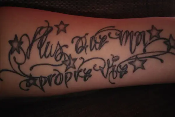 Dezentes Tattoo mit Kindesnamen für einen Mann, verziert mit Sternen und Schnörkeln.