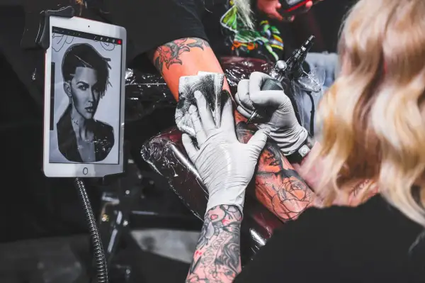Tätowierer arbeitet an einem Porträt-Tattoo, inspiriert von kreativen Tattoos auf einem Tablet.