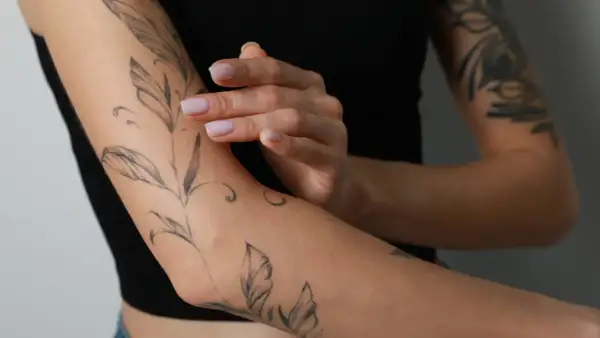 Ein frisches Tattoo mit Blattmotiven ziert den Arm einer Person, die schwarze Kleidung trägt.