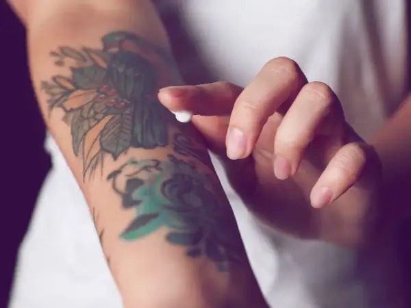 Hand testet Tattoo-Creme auf einem bunten Arm-Tattoo.