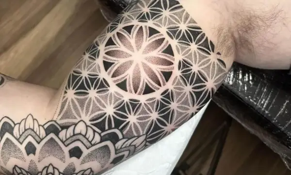 Ein Mann trägt ein geometrisches Tattoo am Oberarm. Das Muster erinnert an eine Blume des Lebens und ist fein gestochen.