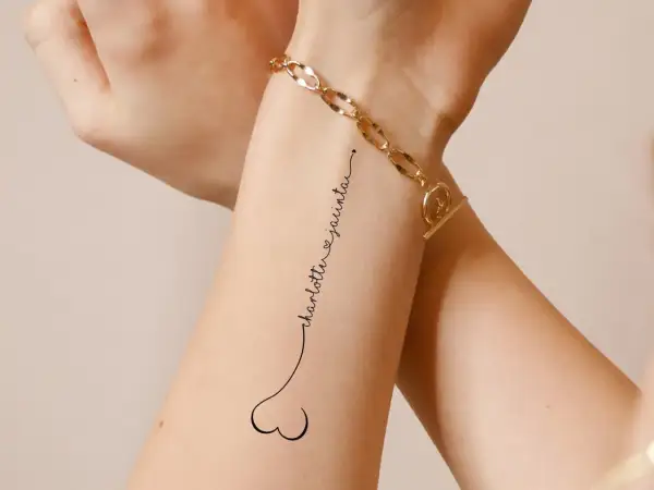 Ein dezentes Tattoo mit den Namen "Charlotte & Jacinta" in geschwungener Schrift, verbunden mit einem kleinen Herz.