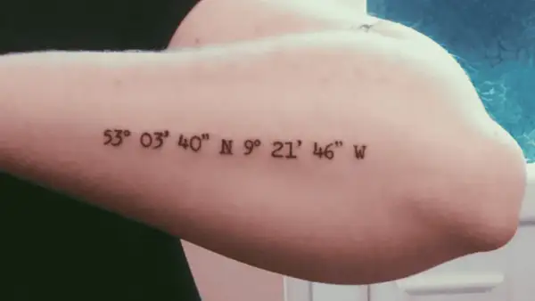 Ein Koordinaten Tattoo in schlichter Schriftart auf dem Oberarm. Die Zahlen markieren einen besonderen Ort.
