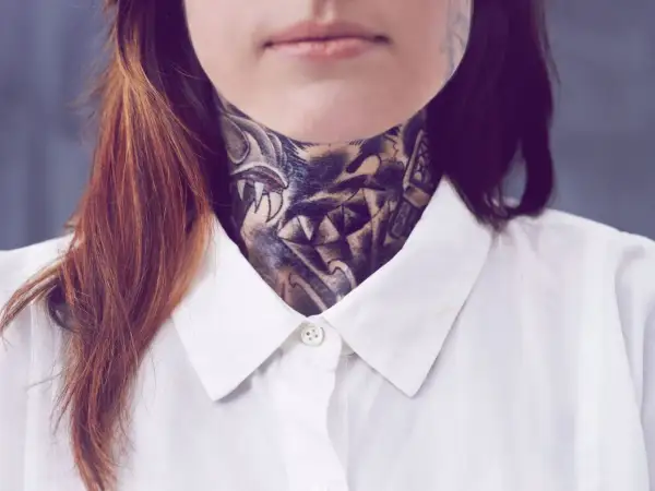 Ein detailreiches, old school Hals Tattoo mit einem Wolfskopf und scharfen Zähnen, bedeckt den Hals einer Person, die ein weißes Hemd trägt.