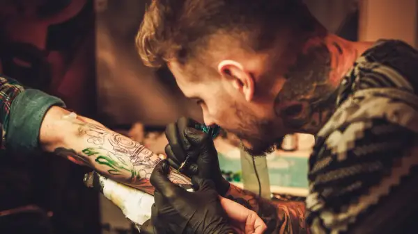 Ein Tätowierer mit vielen Rapper-Tattoos sticht einem Kunden ein neues Motiv auf den Arm.