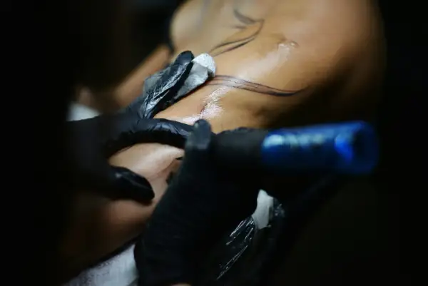Detailaufnahme: Tätowierer mit schwarzen Handschuhen arbeitet an einem Arm. Feine Linien für blackwork tattoos werden auf die Haut gebracht.