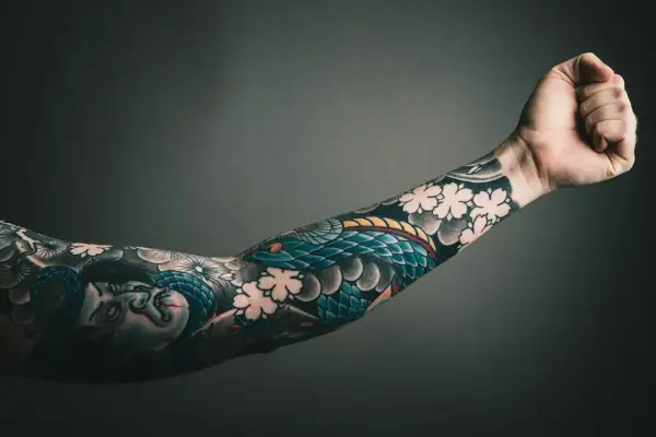 Ein Arm mit einem detailreichen Tattoo, das eine Schlange und Kirschblüten zeigt. Die Botschaft "alles wird gut" ist in diesem Kunstwerk auf der Haut verewigt.