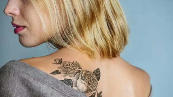 Blonde Frau mit einem Rosen-Tattoo ohne Folie auf der Schulter.
