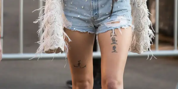 Ein Oberschenkel Tattoo Schriftzug mit einer Rose und einer stilisierten Figur.