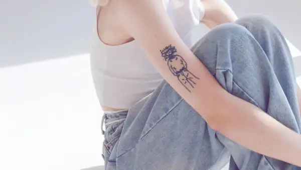 Ein Arm mit einem abstrakten Tattoo, das eine Figur mit einem Kranz darstellt. Die Linien sind klar und dick, ein typisches Merkmal für ein tattoo dicke linien.